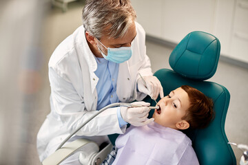 Mature dentist examining little boy's teeth during appointment at dentist's office.