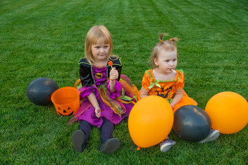 Fototapeta na wymiar little girls with orange and black balloons eating candy from buckets, sitting on grass.