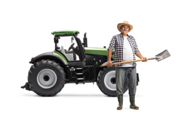 Fototapeta premium Full length portrait of a mature farmer with a shovel in front of a green tractor