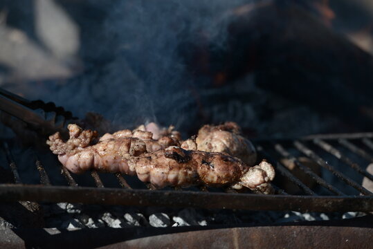 Argentine chinchulines cooking on the coals on a steaming grill