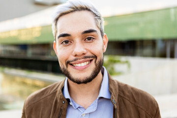 Young hispanic man smiling on camera outdoors - Portrait of happy trendy guy in the city -...