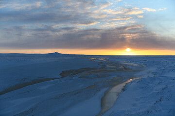 Arctic landscape in winter time. Grass with ice and snow in tundra. Sunset.
