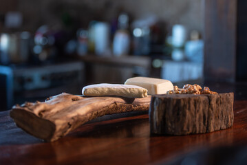 Goat cheese on a rustic wooden tray on a brown table, kitchen in the background.