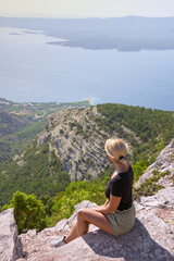 Fototapeta na wymiar A girl sits on the edge of a cliff and looks at the sea