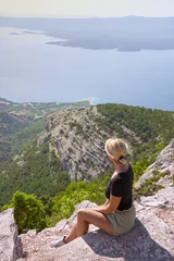 Cercles muraux Plage de la Corne d'Or, Brac, Croatie A girl sits on the edge of a cliff and looks at the sea