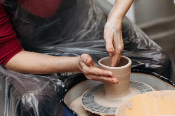 Close up of woman hands forming clay cup spinning on pottery wheel on pottery workshop