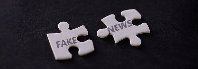 Two white puzzle pieces with fake news text on black background, close up