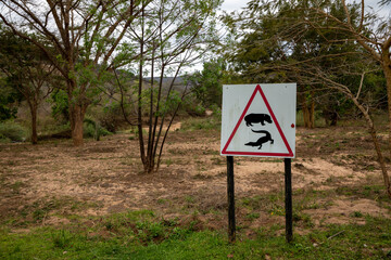 A warning sign that warns people that hippos and crocodiles are in the area. A dry river bed is...