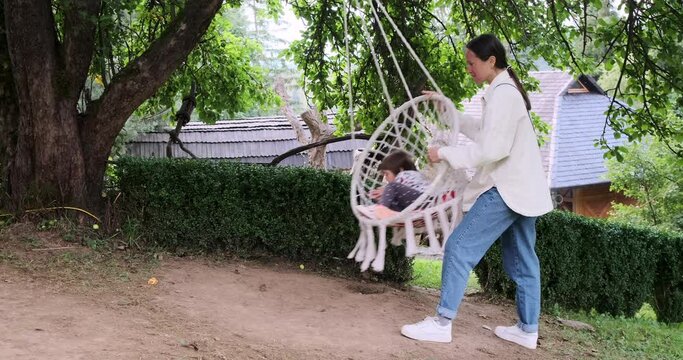 Mother pushing her daughter on swing at park