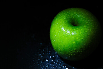 Ripe green apple with water drops on a black background close-up