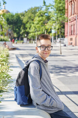 Child teenager boy with  backpack sits and smiles. Online learning, distance education, home schooling.