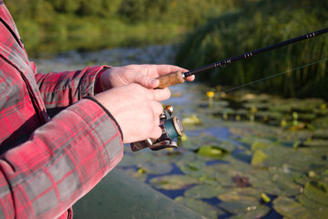 Spinning fishing. Male hands holding a spinning rod on the background of a lake on an autumn sunny day, close-up, soft focus.