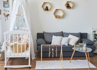 Scandinavian style white interior children's room, bedroom, nursery. Baby cot with ​canopy. Wooden shelves and toys. Children's developmental simulator.