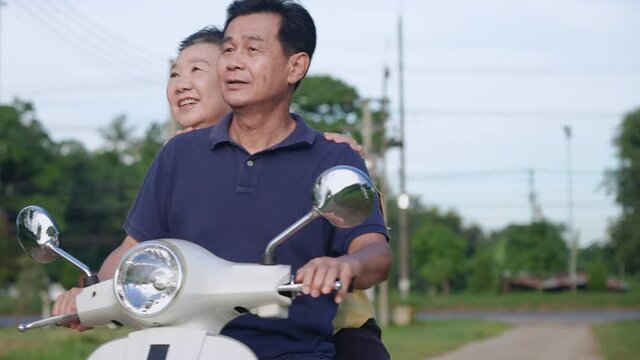 Asian Active Senior Couple Enjoy Riding A White Motorcycle, Elderly People Having Fun With Talking And Pointing Out A View While Sitting Down On Moving Scooter, Happy Old Aged And Lifestyle