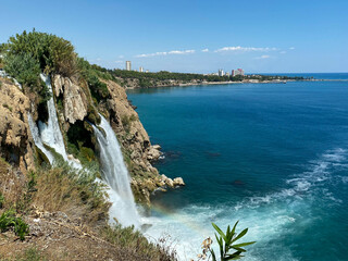 Obraz premium Water falls drop off rocky cliff directly into Mediterranean sea in sunny summer day