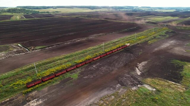 Train transports to peat in freight wagons from peat extraction. Peat extraction site. Harvester at collecting peat on peatlands.