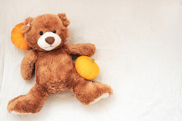 Brown stuffed toy teddy bear with pumpkin on sackcloth fabric texture, flat lay, top view, copyspace. Thanksgiving concept.