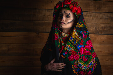 young girl with makeup for the Day of the Dead with a wreath of flowers on his head, wears a lace with flowers scarf looking away. The concept of Halloween or La Calavera Katrina