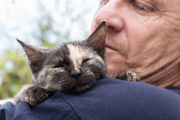 A kitten with a strip on its nose sleeps on the shoulder of an adult man. Love for pets
