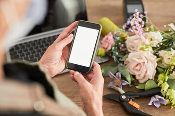 Close up of female small business owner using smartphone with blank screen while managing flower shop, copy space