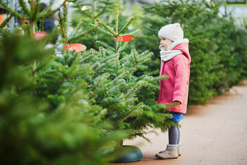 Happy cheerful preschooler girl on Christmas tree market selecting a tree