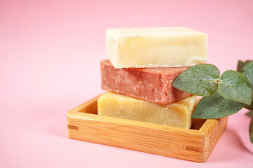 Natural handmade organic soap bars stack on wooden tray with euacalyptus leaves. Close up against a pink background with negative copy space.