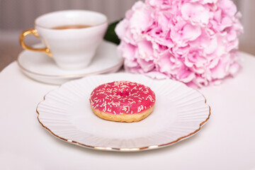 Cup of tea, sweet strawberry donut on golden plate with hydrangea flower