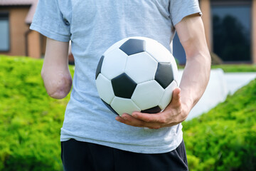Full length young caucasian man with amputated arm, holds of soccer ball while standing on the lawn...