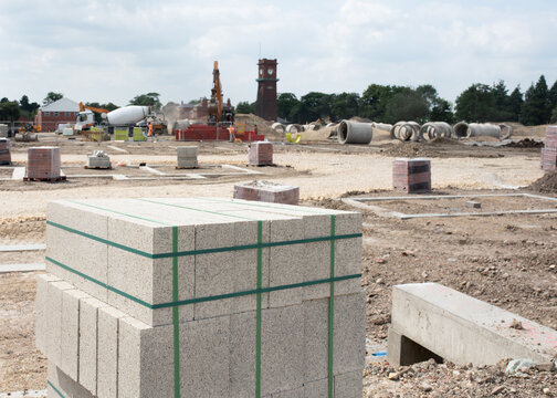 Concrete blocks and bricks  on new housing development construction site and  next to house foundation,  while deep drainage works using concrete pipes of the big diameter continues in the background 