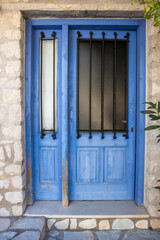 Fototapeta na wymiar Entrance closed door with blue shutters, glass window and iron-shod details. Greek traditional house with stone walls. Summer travel locations architecture