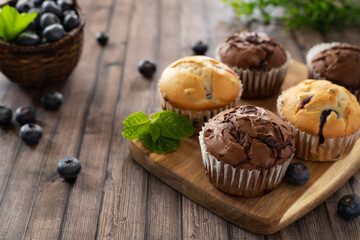 Chocolate and blueberry muffins on a wooden board decorated with mint and berries, side view