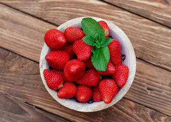 red strawberries in a bowl on wooden table in the garden	