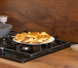 Freshly baked pancakes in a white plate on the gas stove in the kitchen.