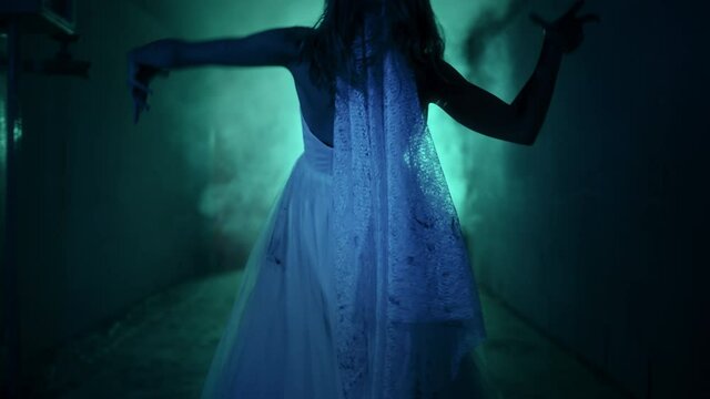 Dead zombie woman scaring in dark corridor close-up. Creepy bride wearing wedding dress with veil. Deceased fiancee returned to life. Horrible klip on halloween. Haunted house. 