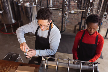 Caucasian man wearing an apron fastening lid on bottle of gin at gin distillery