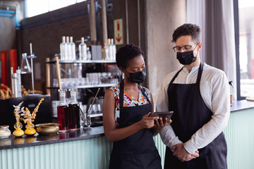 Diverse man and woman wearing aprons using digital tablet at gin distillery