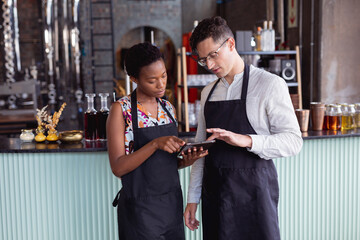 Caucasian man and african american woman wearing aprons using digital tablet at gin distillery