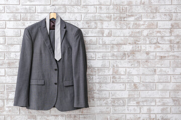 Hanger with stylish suit and necktie hanging on brick wall