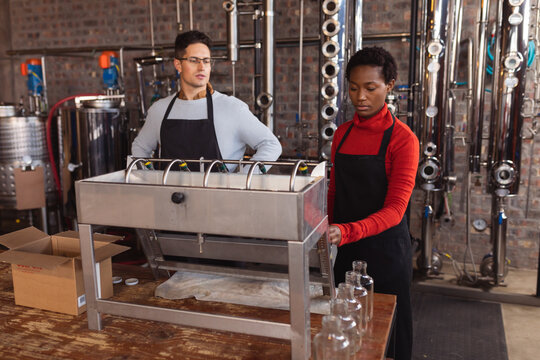 Caucasian man and african american woman using machinery at gin distillery