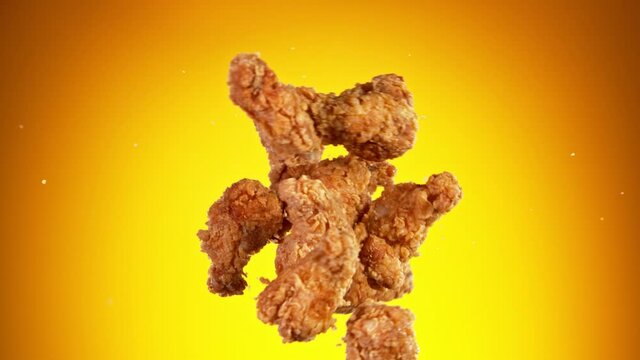 Super slow motion of flying fried chicken pieces hitting in the air, isolated on golden background. Filmed on high speed cinema camera, 1000fps