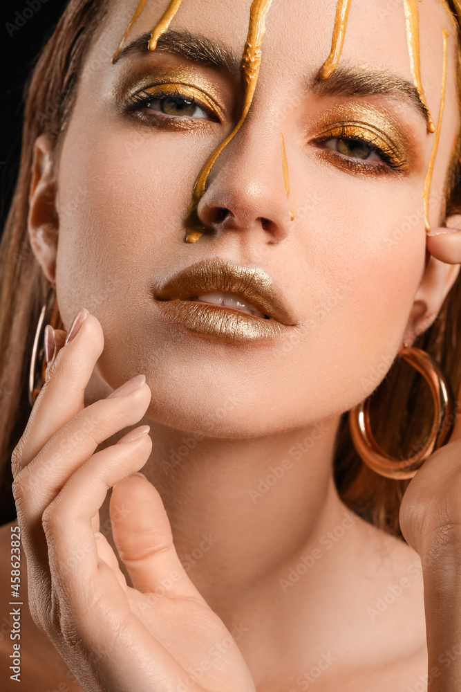 Sticker Beautiful young woman with  golden paint on her face against black background