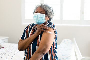 Unhappy senior african american woman wearing face mask with plaster on arm after vaccination