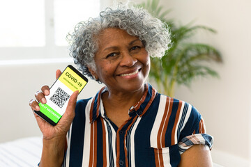 Happy senior african american woman showing covid vaccine passport on smartphone