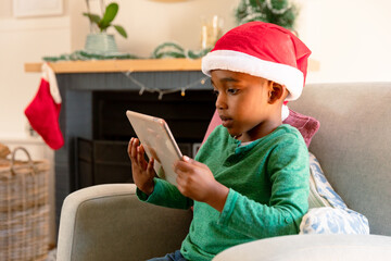 African american boy wearing santa hat and using tablet at christmas time