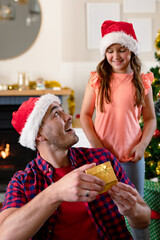Surprised caucasian father wearing santa hat receiving present from his daughter at christmas time