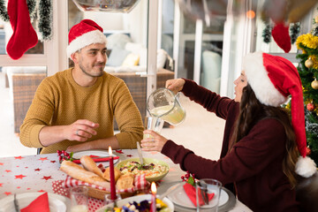Happy caucasian couple having christmas meal, pouring beverage in to glass