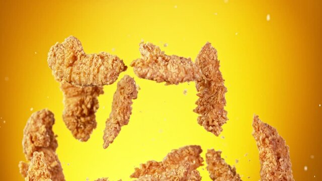 Super slow motion of flying fried chicken pieces on golden background. Filmed on high speed cinema camera, 1000fps. Speed ramp effect.