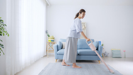 部屋の床に掃除機をかける若い女性・主婦