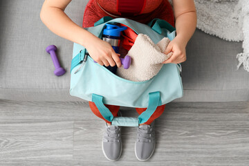 Woman in sportswear sitting on sofa and preparing bag for training