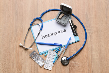 Clipboard with text HEARING LOSS, stethoscope and pills on light wooden background